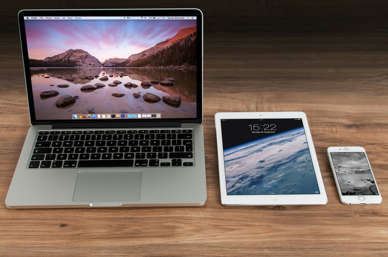 A MacBook, an iPad and an iPhone side by side on a wooden desk