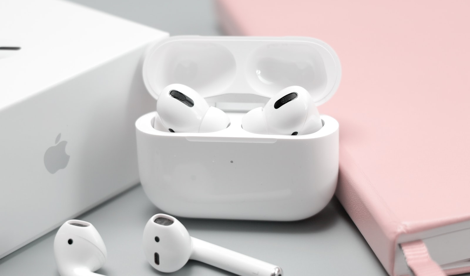 Unos AirPods Pro con su estuche de carga sobre un fondo pastel