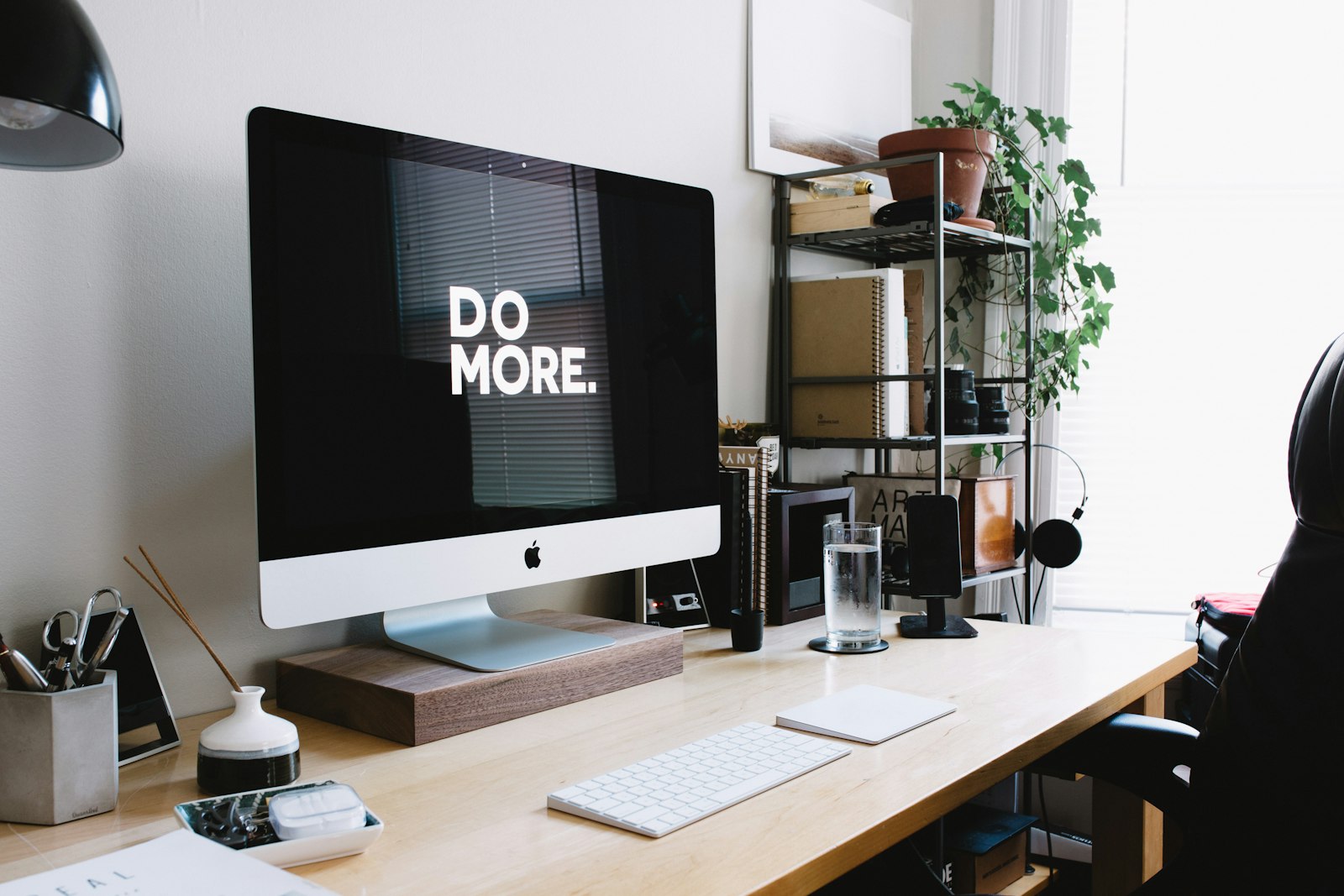 An iMac on a wooden desk in a bright office, with a keyboard and plants
