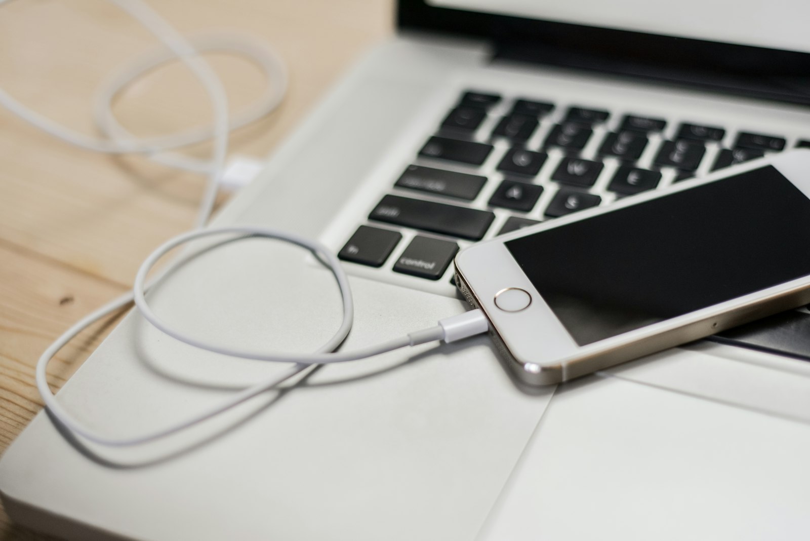 An iPhone connected by a white cable next to a MacBook keyboard