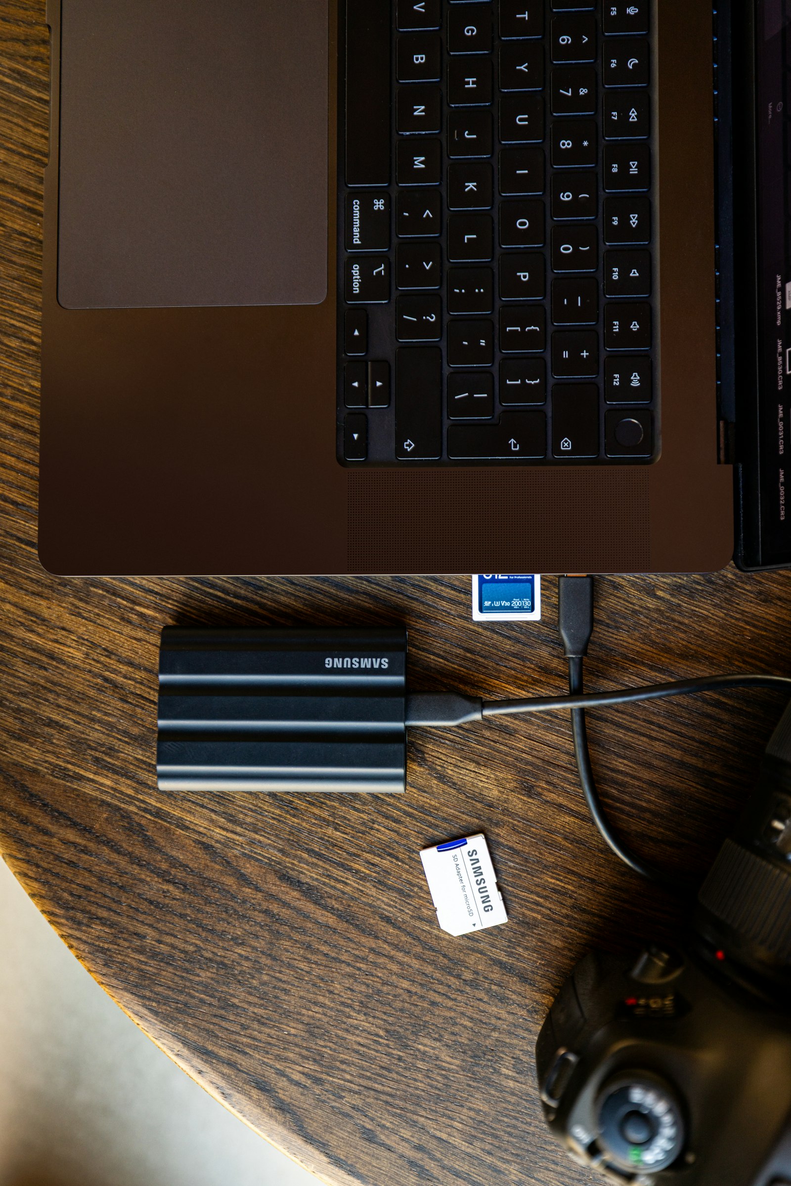 A portable external SSD connected by cable to a laptop on a wooden desk