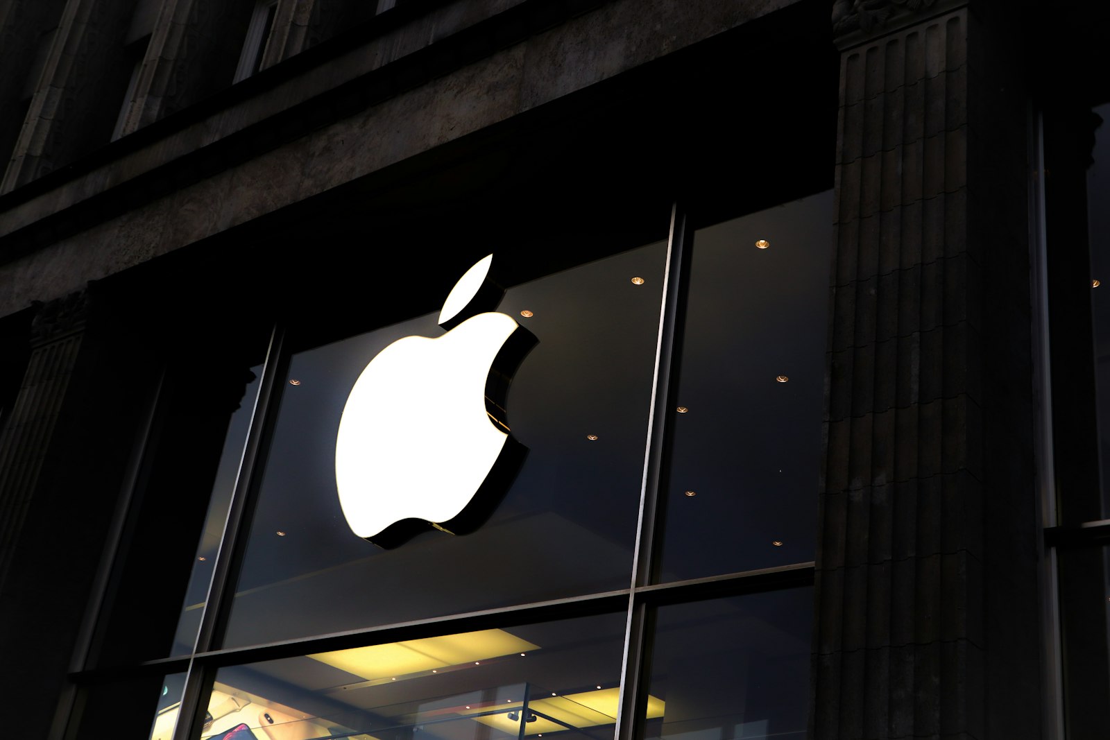 Illuminated Apple logo on the dark glass facade of an Apple Store at night
