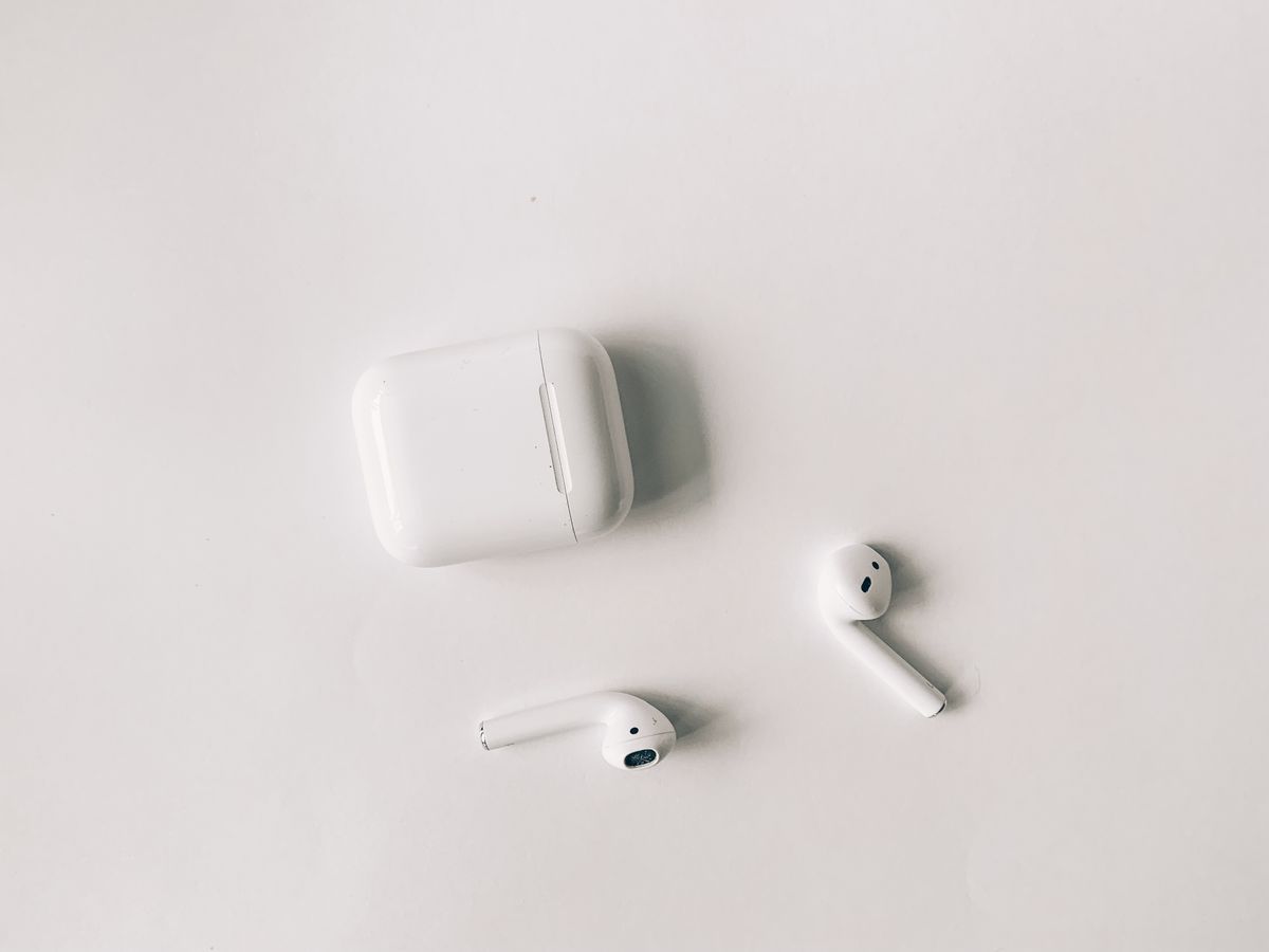 Photo of white AirPods and their charging case on a white surface; the camera-equipped model has not been shown publicly
