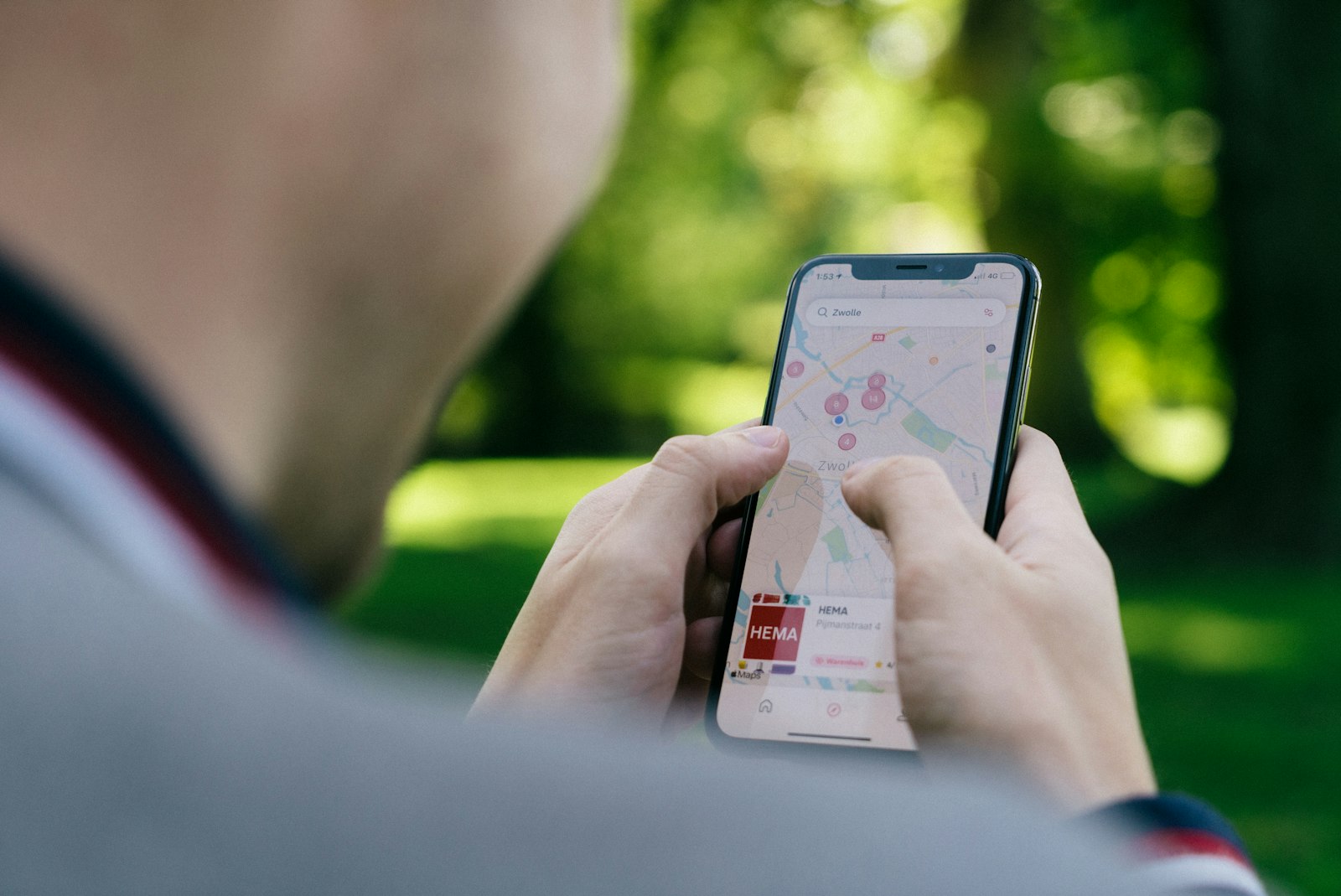 Una persona sostiene un iPhone con una búsqueda en Apple Mapas y la ficha de un comercio local en la parte inferior.