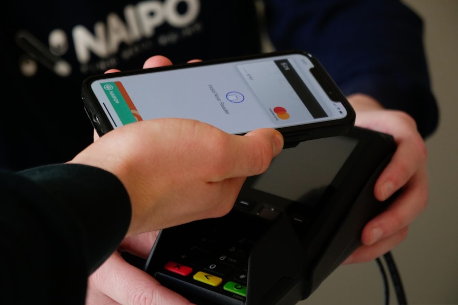 An iPhone held above a contactless payment terminal showing Apple Pay; the pictured interface predates the announced redesign.