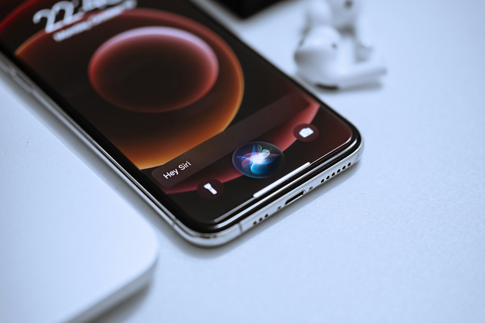 An iPhone displaying the Hey Siri prompt beside AirPods and a Magic Mouse