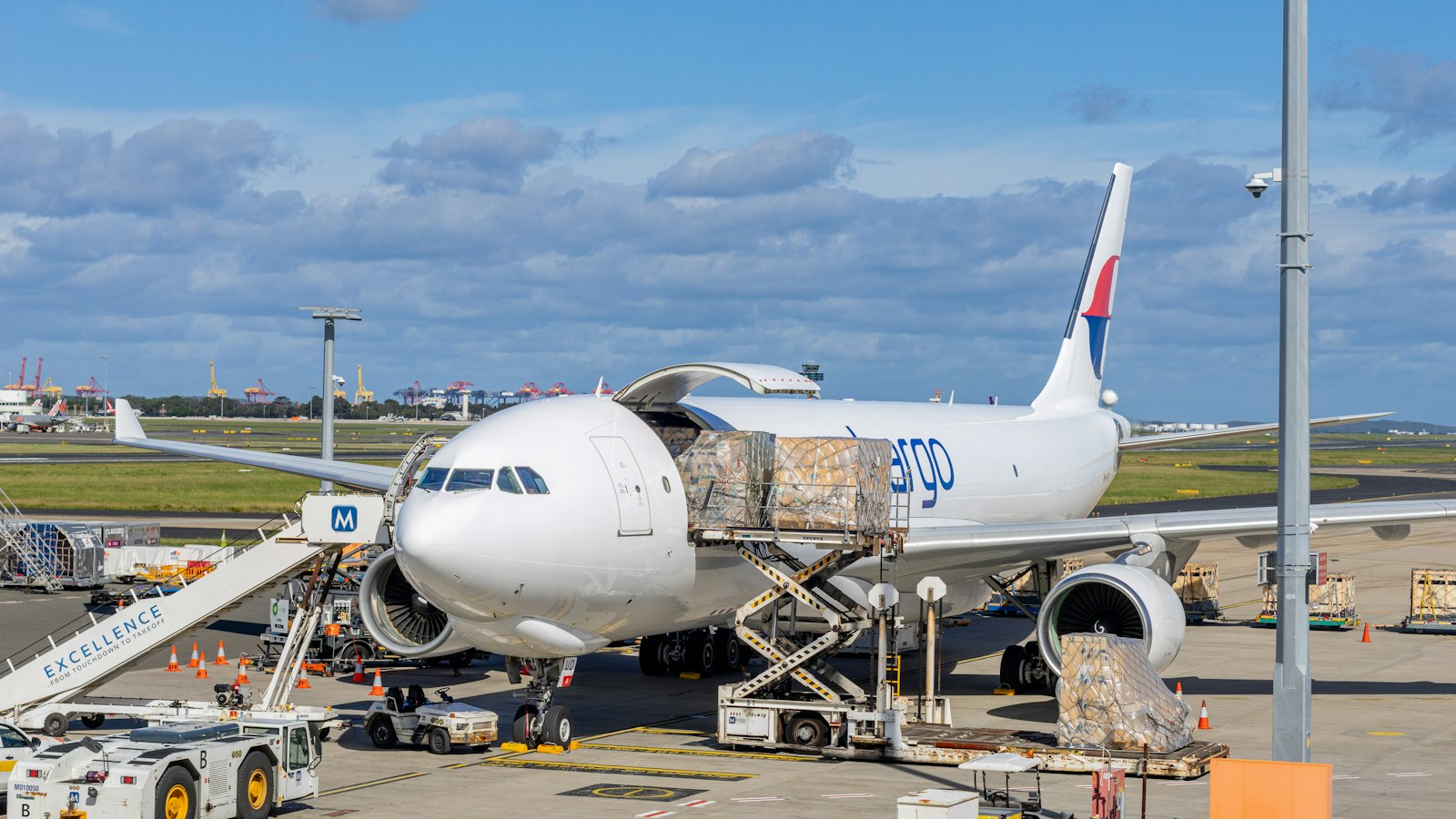 A cargo pallet is loaded through the main-deck door of a white cargo aircraft on an airport apron.