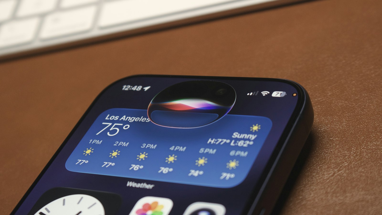 The colored Siri glow is active in the Dynamic Island of an iPhone resting on a desk.