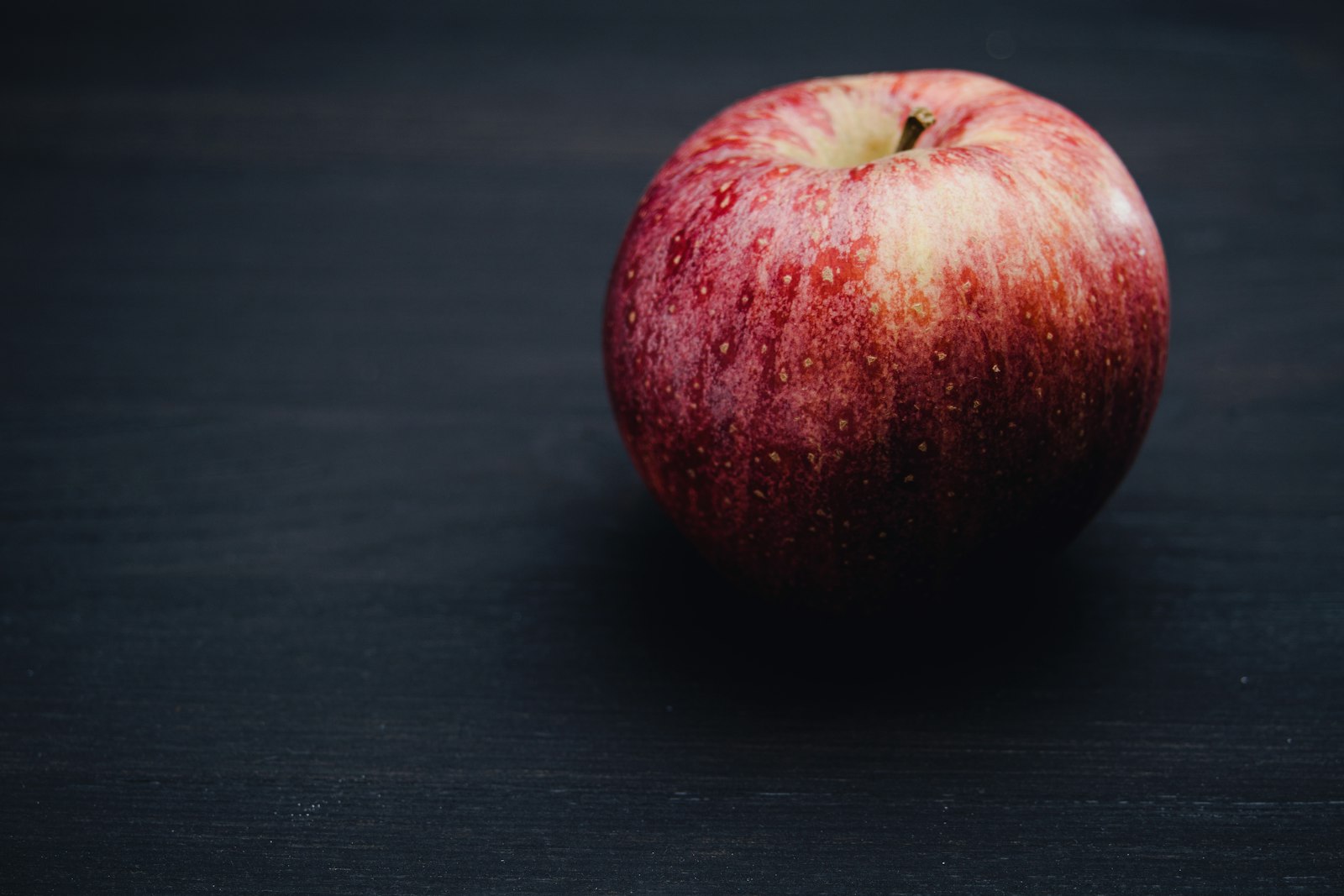 Une pomme rouge posée sur une surface sombre